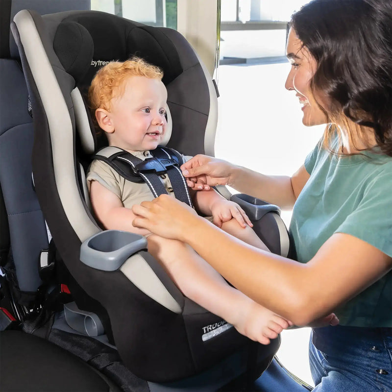 A mom is placing her child in the Baby Trend Trooper SLIM 3-in-1 Convertible Car Seat 