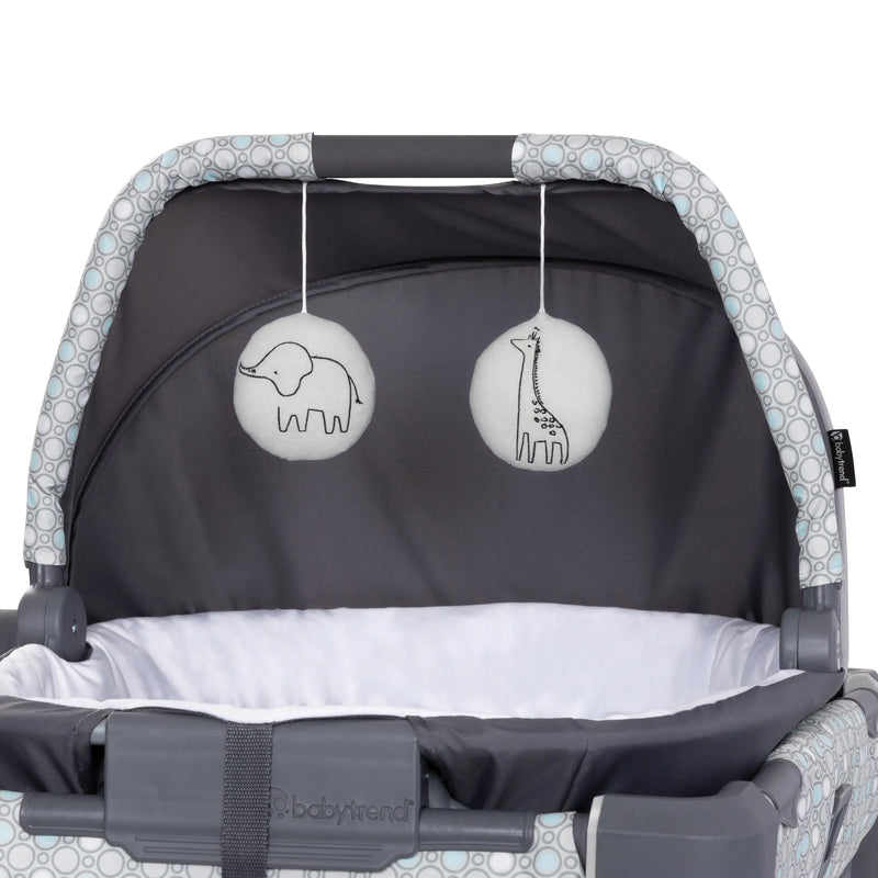 The portable cradle has two hanging toys on the canopy of the Baby Trend Nursery Den Playard with Rocking Cradle