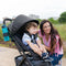 A mom is outdoor with her child sitting in the Baby Trend Tango Mini Stroller