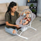 A mom is watching her child sit in the Baby Trend Sit N' Sway Portable Swing