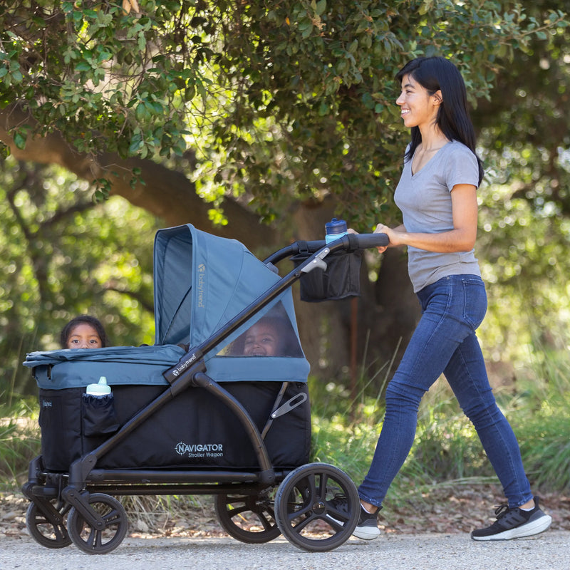 Mom is pushing her two children in the Baby Trend Navigator 2-in-1 Stroller Wagon