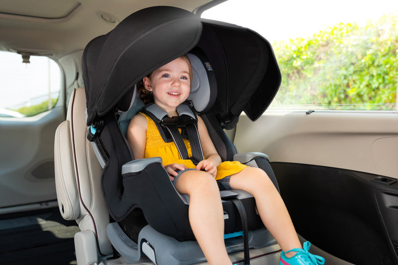 A child sitting in the Cover Me Convertible Car Seat with the canopy blocking the sun