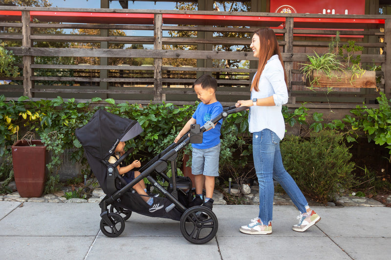 A child sitting in the front seat with another standing on the rear of the Baby Trend Morph Single to Double Modular Stroller