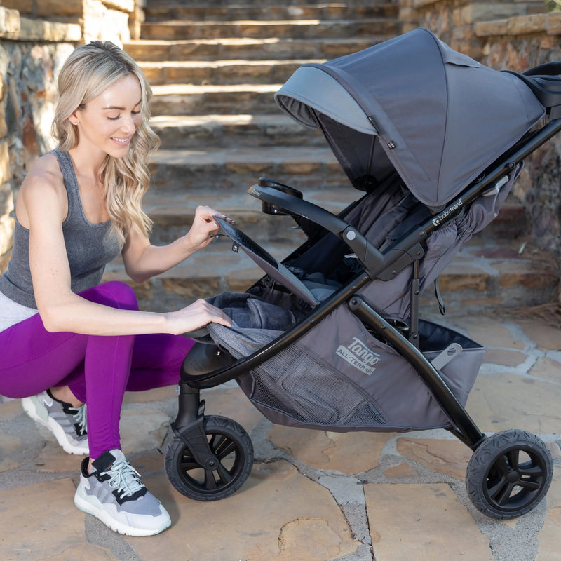 Mother is accessing the storage basket from the front of the Baby Trend Tango 3 All-Terrain Stroller Travel System