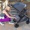 Mom is accessing the storage basket from the rear of the Baby Trend Tango 3 All-Terrain Stroller Travel System