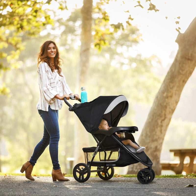 Mom is strolling her child outdoor at the park with the Baby Trend EZ Ride PLUS Stroller Travel System